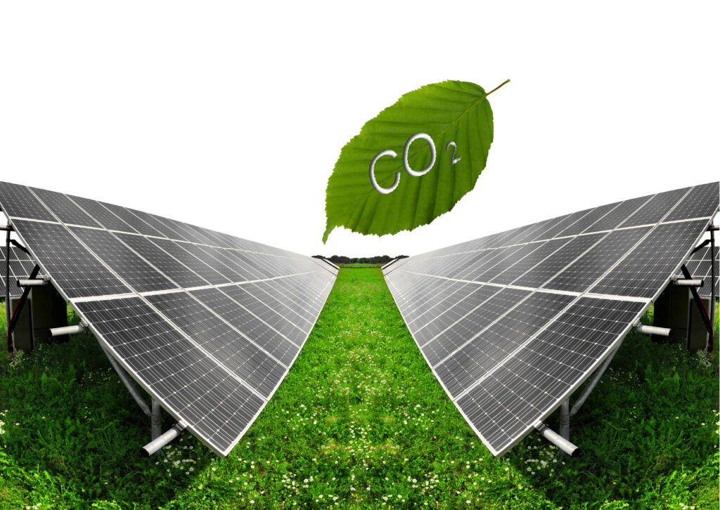 placas solares uma de frente para outra sobre gramado verde e follha verde em cima com o símbolo do carbono